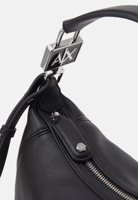 Sac à main en cuir noir avec quincaillerie argentée, arborant un fermoir en logo et des détails de fermeture éclair. Texture lisse avec une forme arrondie.