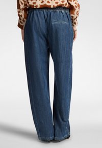 Niebieskie dżinsowe spodnie z elastycznym paskiem, luźnym krojem i jedną tylną kieszenią z delikatnymi detalami stębnowania.