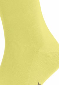 Elastische Knöchelsocke aus leuchtend gelbem Stoff, die eine glatte Textur und ein dezentes Rippmuster zeigt, mit kleiner grauer Markenkennzeichnung am Bund.