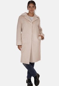 Cappotto in faux fur beige con colletto a contrasto, maniche lunghe e taglio dritto. Presenta tasche laterali e una superficie morbida e testurizzata.