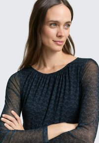 Marineblauwe blouse met doorschijnende lange mouwen, gegarnde halslijn en contrasterende lichtblauw gestikte patronen. Gladde textuur en relaxte pasvorm.