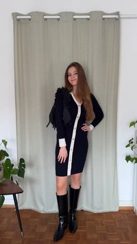 Marineblauwe ribbeljurk met witte knopenlijst en gerimpelde zwarte accenten op de schouder. Zwarte kniehoge laarzen. Lichtgroene achtergrond.