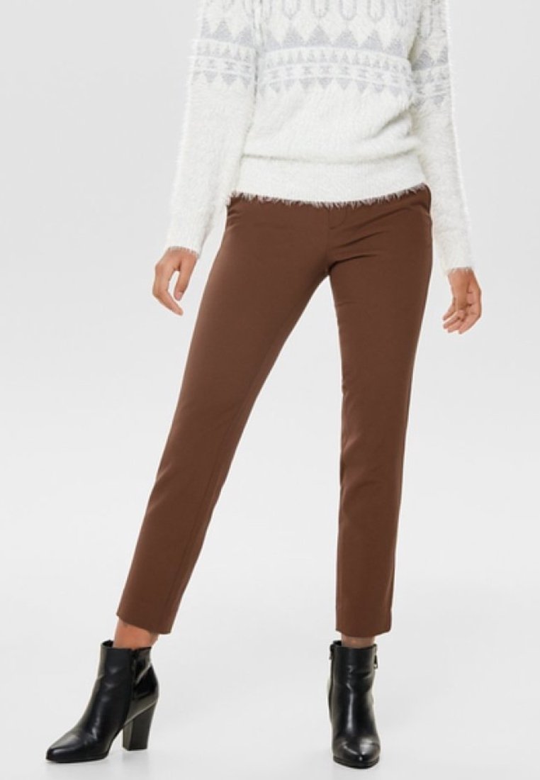 Bruna snäva byxor i ett glansigt material, tillsammans med svarta ankelstövlar. Outfiten kompletteras av en vit, texturerad tröja.