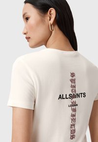 T-shirt en coton crème à manches courtes, avec le texte noir "ALLSAINTS LONDON" et des éléments de design texturé en rose au dos.