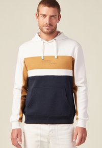 Felpa con cappuccio in blocchi di colore bianco, senape e blu navy. Texture morbida, tasca frontale e branding embossato sul petto.
