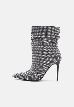 Zwarte enkellaarsjes met hoge hakken van stof, bedekt met zilveren rhinestones, met een slouchy ontwerp en een spitse neus. Soepele textuur, slanke silhouet.