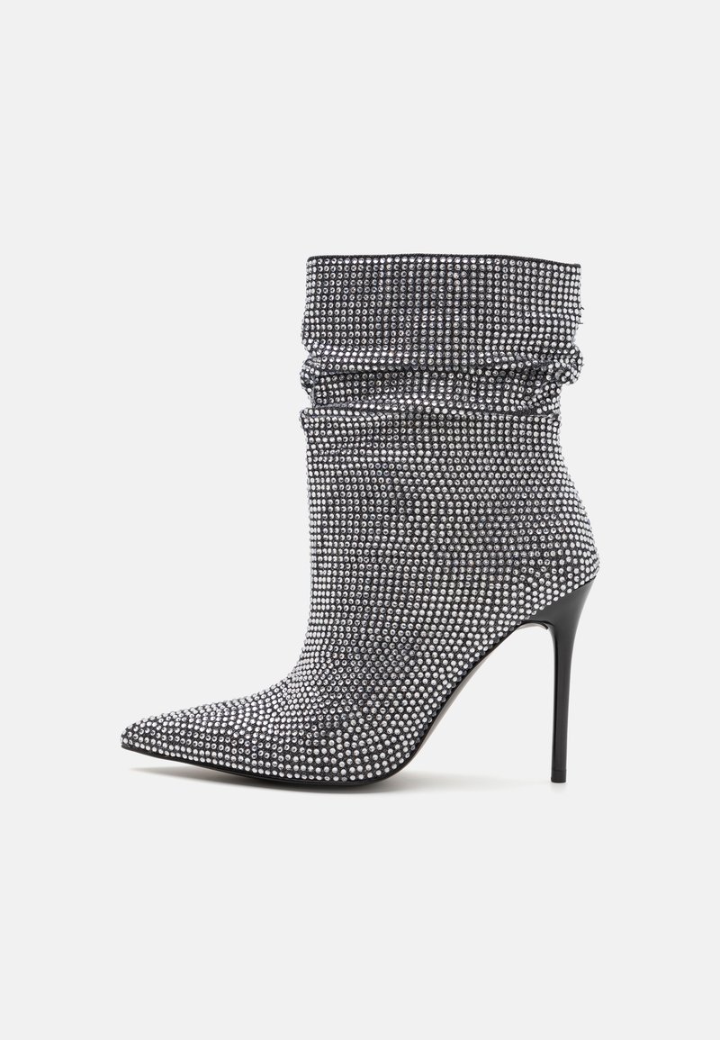 Botín de tacón alto en tejido negro, cubierto de strass plateados, con un diseño holgado y punta afilada. Textura suave, silueta elegante.