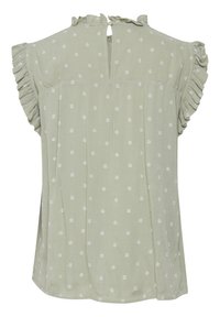 Blouse vert clair à pois blancs. Dotée de manches à volants et d'une fermeture en keyhole au dos. Tissu doux et texturé avec une coupe ample.