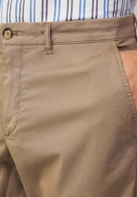 Chino beige chiaro realizzati in tessuto morbido, dotati di un cinturino con bottone, tasche laterali e cuciture rifinite con cura.