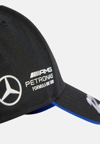 Sort kasket med en buet skygge, prydet med hvide logoer: AMG og Petronas. Blå underside af skyggen, tekstureret stof og justerbar rem.