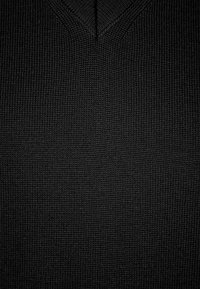 Schwarzer Strickpullover mit V-Ausschnitt-Design. Der Stoff weist ein strukturiertes Muster auf und präsentiert eine feine Webart sowie eine gleichmäßige Farbgebung.