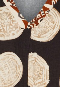 Svart tyg med cirkulära beige mönster, inklusive abstrakta designer och spiralmotiv. V-ringning framhävd av en tryckt kant.