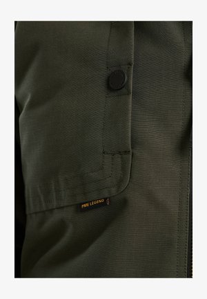Groene stoffen jas met een gestructureerd oppervlak, een opvallende zwarte knop en een zichtbaar PME Legend label met gele letters.