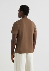 T-shirt marrone a maniche corte realizzato in tessuto morbido, con collo rotondo e vestibilità rilassata, abbinato a pantaloni bianchi a gamba larga.