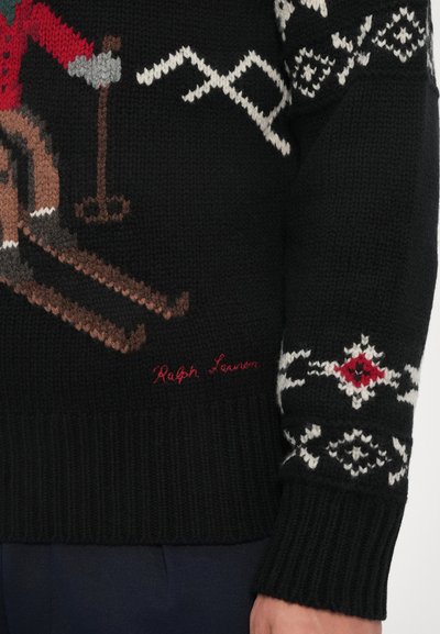 Črn pleten pulover z dizajnom smučanja v odtenkih rdeče, rjave in sive, z belimi geometrijskimi vzorci na rokavih. "Ralph Lauren" je izvezena v rdeči barvi.