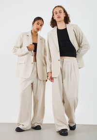Blazers beige ajustés à deux boutons, associés à un pantalon beige ample ; tops noirs ajustés en dessous. Texture lisse, minimalisme.