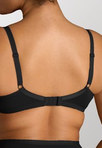 Reggiseno nero con spalline regolabili, texture liscia e chiusura a gancio sul retro, con piccoli accenti rotondi sulle spalline.