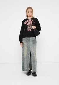 Sweatshirt preto com estampa rosa, combinado com uma saia de ganga longa em padrão de serpente com uma fenda lateral e sapatos pretos robustos.