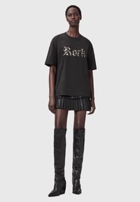 Mustat t-paidat, joissa on kulunut "Rarh" -teksti, yhdistettynä mustaan laskoshameeseen ja polvimittaisiin mustiin nahkabootseihin, luoden kerroksellisen ilmeen.