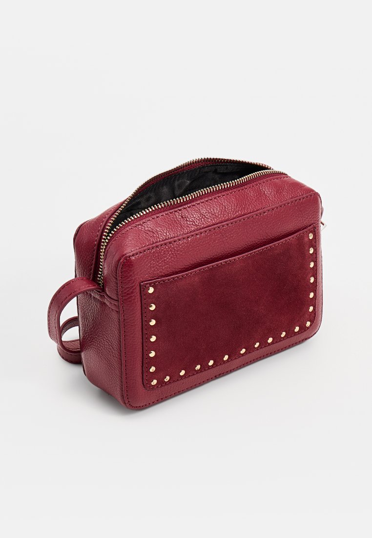 Burgundowa skórzana torba o teksturowanym wykończeniu, z akcentami w postaci złotych ćwieków i zamkiem błyskawicznym. Kompaktowy prostokątny kształt z uchwytem do przenoszenia.
