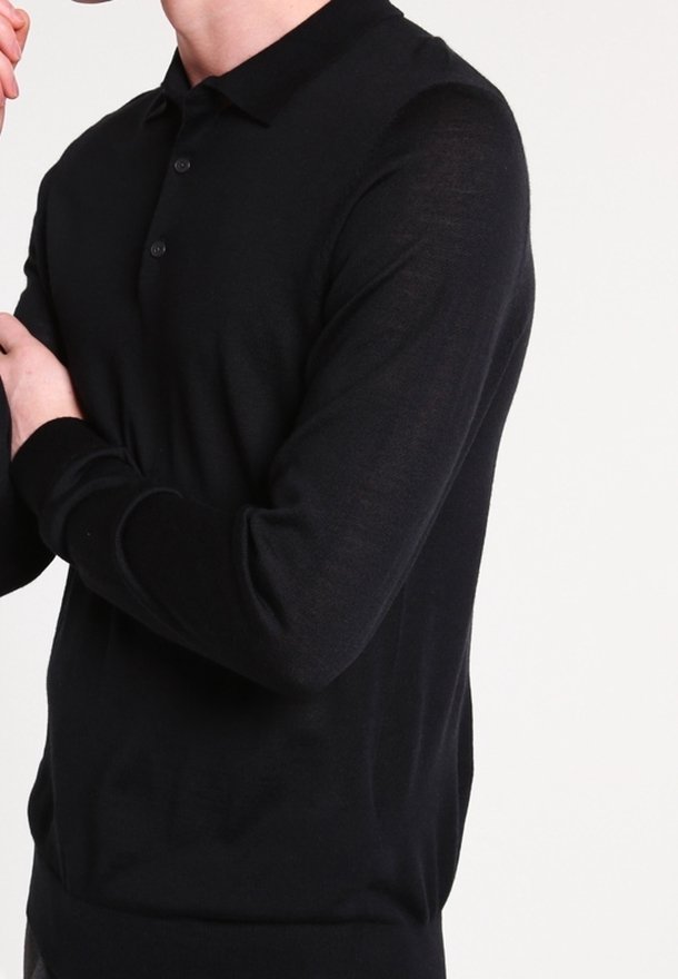 Personne portant un polo noir à manches longues avec un col boutonné, présenté du cou jusqu'aux hanches sur fond blanc.