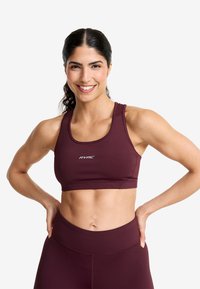 Mörkröd sport-bh med en åtsittande passform, med rund halsringning och "RVRC"-logotypen i vitt. Slät tyg och minimal sömnadsdetalj.