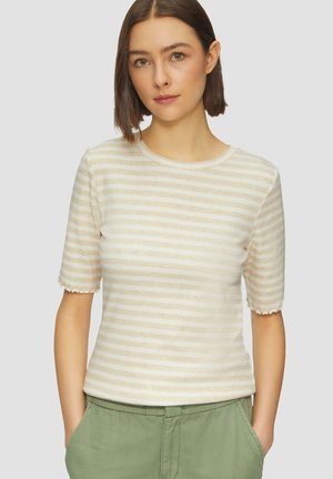 Crème top met korte mouwen met horizontale beige strepen, ronde hals, gegolfde mouwranden en een zachte textuur. Draagt bij groene broek.