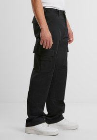 Svarta cargobyxor med flera sidofickor, avslappnad passform, tillverkade av ett slitstarkt material, kombinerade med vita sneakers för kontrast.