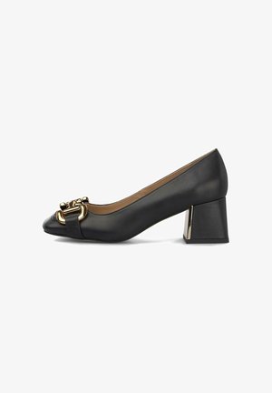 Zapatos de charol negro con tacón bloque y punta redondeada, que presentan un acento de metal en tono dorado en la parte frontal y una textura suave.