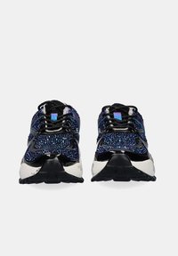 Un par de zapatillas brillantes negras y azules con suelas blancas, vistas desde el frente sobre un fondo gris claro.