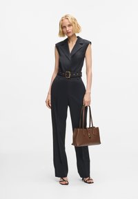 Fekete ujjatlan overál övvel és arany kiegészítőkkel, barna kézitáskával párosítva. Hosszú, bő szabású nadrág és lapos szandál.