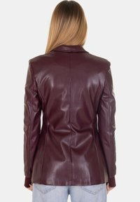 Blazer bordeaux in ecopelle con taglio sagomato, rever a lancia e texture liscia. La parte posteriore presenta cuciture verticali e dettagli minimali.