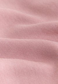 Nahaufnahme von rosa geripptem Stoff mit weichen Falten und strukturierten diagonalen Linien, die das Strickmuster hervorheben.