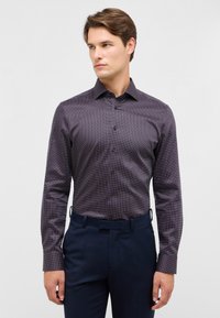 Camicia a maniche lunghe, aderente, di colore viola scuro con un fine motivo a pois. Presenta una texture liscia, apertura con bottoni sul davanti e colletto, abbinata a pantaloni scuri.