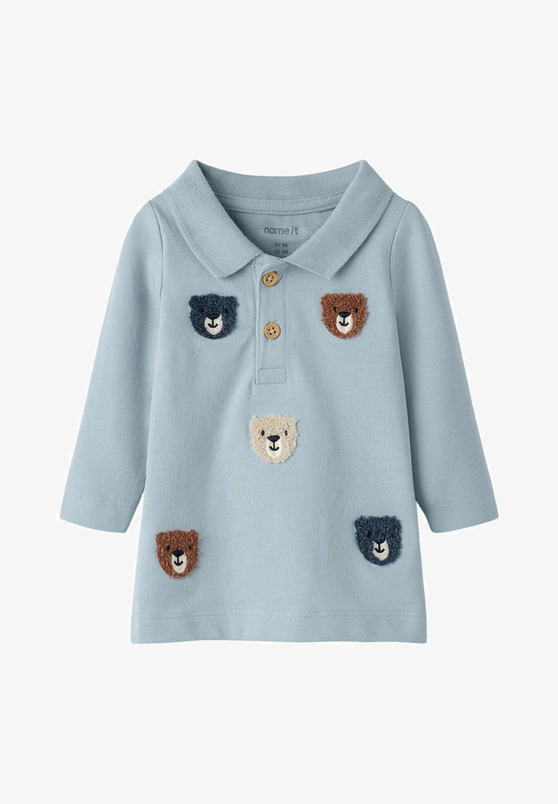 Polo à manches longues bleu clair pour tout-petit avec col, deux boutons en bois et cinq écussons colorés en forme de visage d'ours en peluche sur le devant.