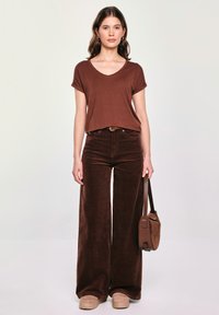 Brązowy krótki top z dekoltem w serek w połączeniu z szerokimi spodniami z brązowego sztruksu. Dodatki to brązowy pasek i mała brązowa torebka.