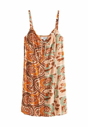 Personne blonde aux cheveux ondulés portant une robe à motifs aux tons naturels avec un motif toucan coloré dans le dos.
