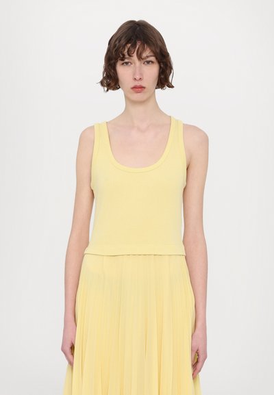 Gul tanktop med brede stropper og scoop halsudskæring, parret med en plisseret nederdel i matchende gult stof. Glat tekstur og afslappet design.