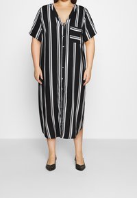 Czarna i biała, w paski, maxi sukienka z dekoltem w serek, krótkimi rękawami, z przodu zapinana na guziki i z kieszonką na piersi. Gładki materiał i luźny krój.