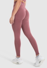 Leggings aderenti color marsala realizzati in materiale elastico, con una vita alta e una texture liscia, abbinati a sneakers sportive bianche.