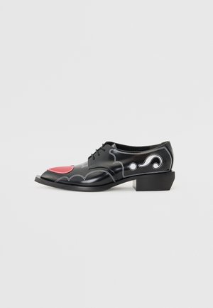 Black leather shoes with a block heel, featuring red accents and white stitching in decorative patterns. Designed with rounded toe and lace-up closure.
