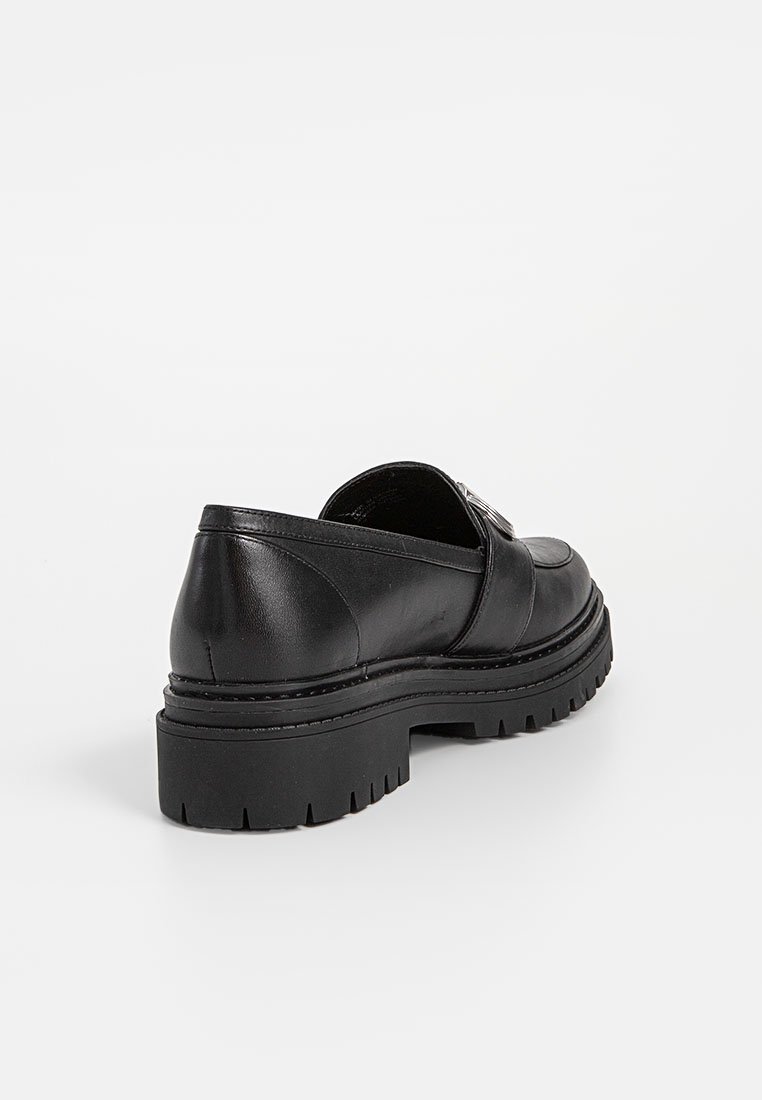 Scarpa in pelle nera con suola spessa, forma arrotondata e cuciture in vista. Presenta un design a intaglio e un accentuato dettaglio metallico.