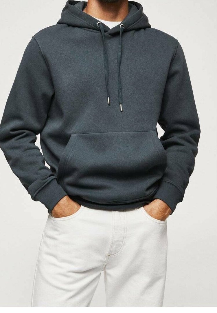 Homme portant un sweat à capuche gris foncé avec une poche avant et des cordons blancs, assorti à un pantalon blanc, mains dans les poches.