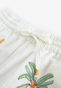 Baltos raišteliu surišamos šortai, pagaminti iš tekstūruoto audinio, su elastiniu juosmeniu ir žalių palmės medžių siuvinėjimu su oranžiniais akcentais.