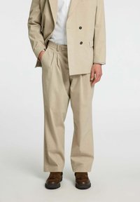 Beżowy garnitur double-breasted z subtelnym wzorem w paski, luźne spodnie oraz brązowe, fakturowane buty. Skrojony z funkcjonalnymi kieszeniami.