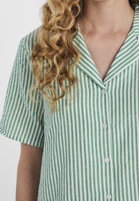 Zielona i biała w paski koszula z krótkim rękawem, z kołnierzykiem i zapięciem na guziki, wykonana z lekkiego materiału o lekko teksturowanym wykończeniu.