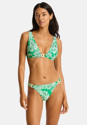 Kobieta ubrana w zielone bikini z białym kwiatowym wzorem i beżowymi detalami z łańcuszków na górze i na dole, stojąca na białym tle.