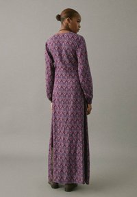 Rochie lungă, de culoare purpurie, cu un model floral, mâneci lungi, dungi verticale și o fanta laterală. Prezintă o talie talie strânsă și un decolteu rotund.