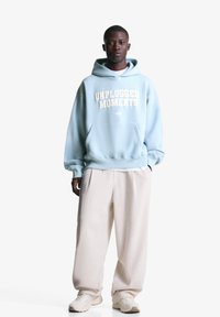 Lys blå hoodie med "UNPLUGGED MOMENTS" trykt i hvid, parret med cremefarvede corduroybukser og beige sneakers. Glat tekstur.