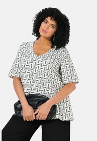Top de manga corta con escote en V en blanco con patrón de zigzag negro; combinado con un bolso de mano negro texturizado y pantalones negros.